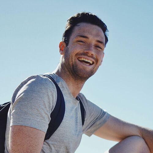 Junger Mann mit T-Shirt und mit Rucksack bei blauem Himmel