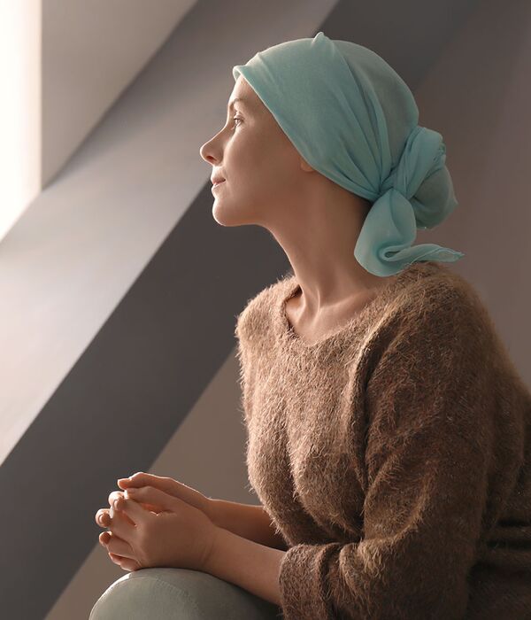 Cancer patient with a turquoise headdress looks out of the window